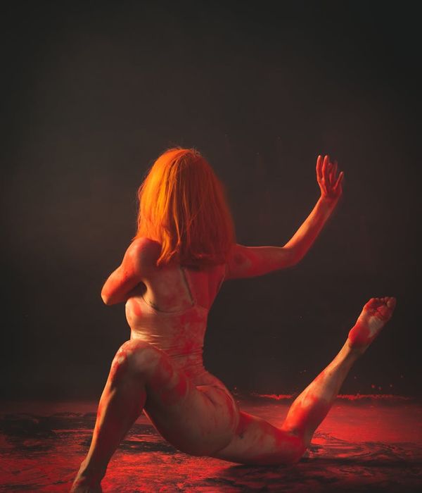 Woman performing a fluid yoga pose in a dark room with cyan highlights.